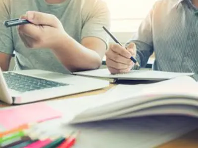 one person writing in a notebook and one person working on a laptop